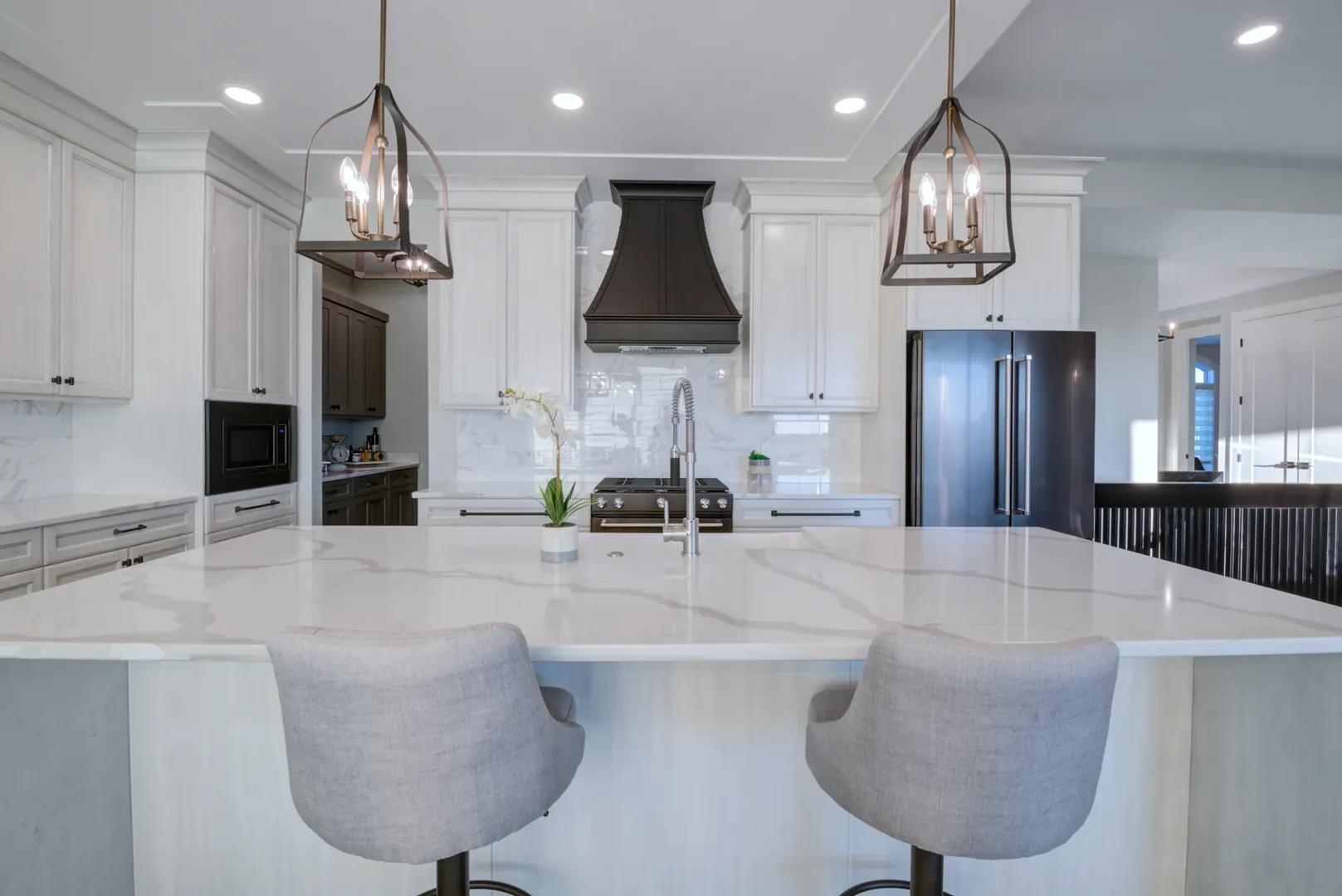 Kenco kitchen with white cabinetry, a stone island and sculptural pendant lights